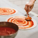 Tomatensoße wird auf Pizza verteilt